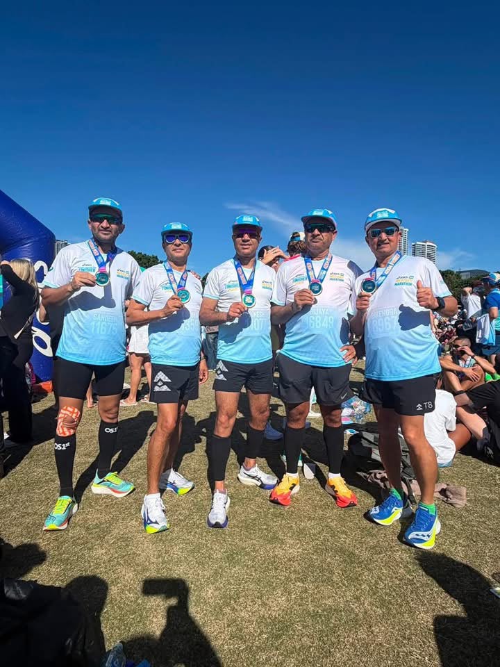 Five marathon finishers in blue caps showing their medals